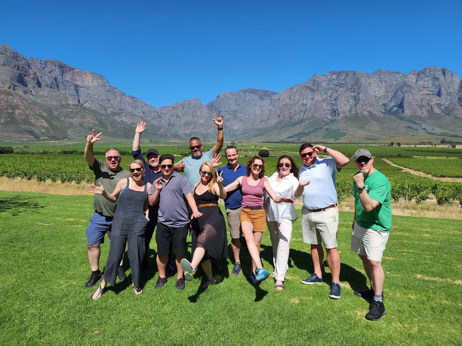 The Baobab Wines team celebrating together on the lawn of a Cape winelands estate, vineyards and mountains behind