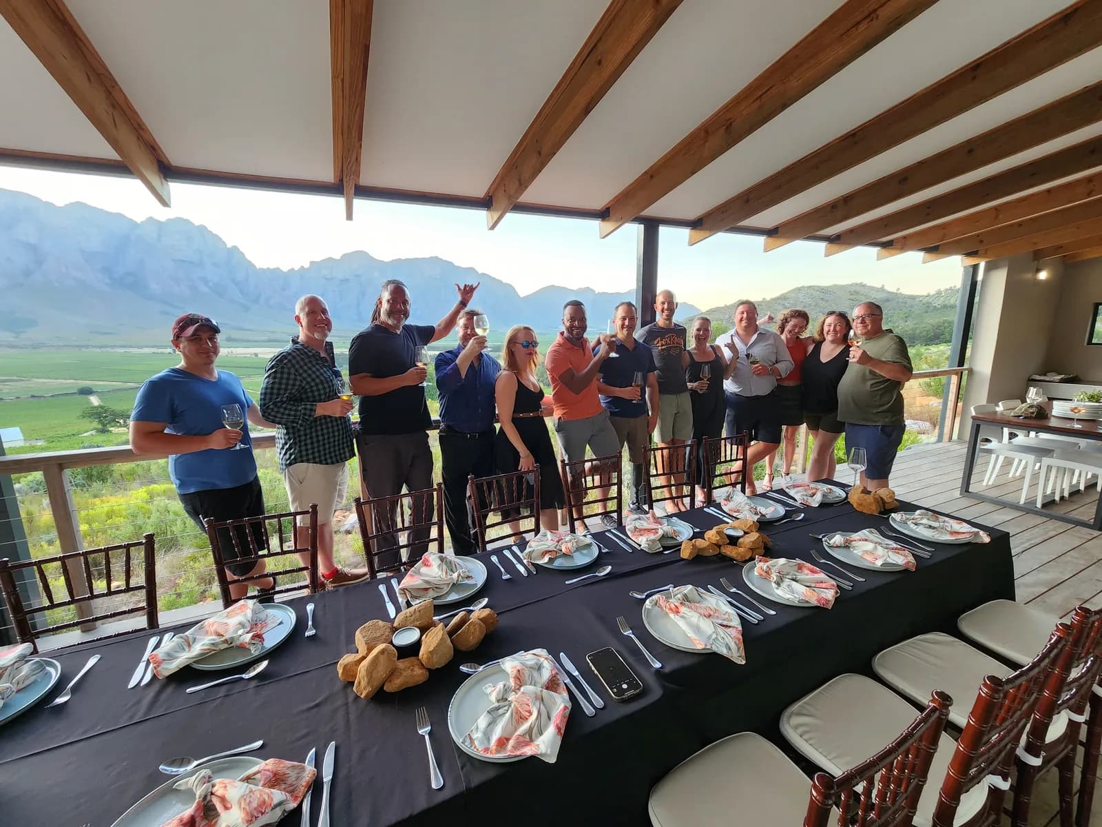 Raising a toast around a dinner table set on a deck overlooking the winelands at dusk