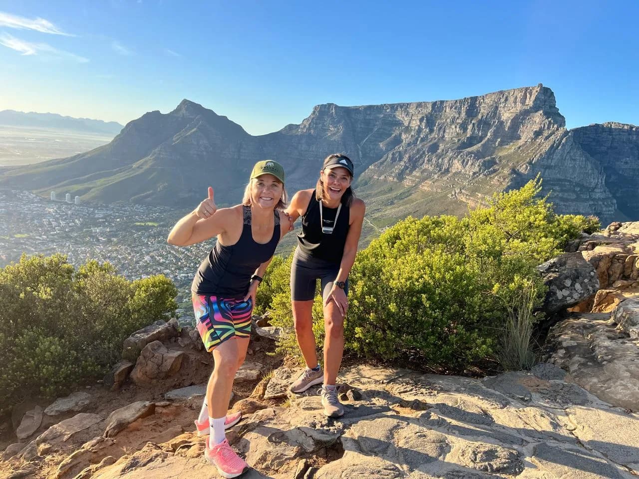 Two travellers on a rocky Lion's Head trail with Table Mountain, Devil's Peak and the city bowl behind them
