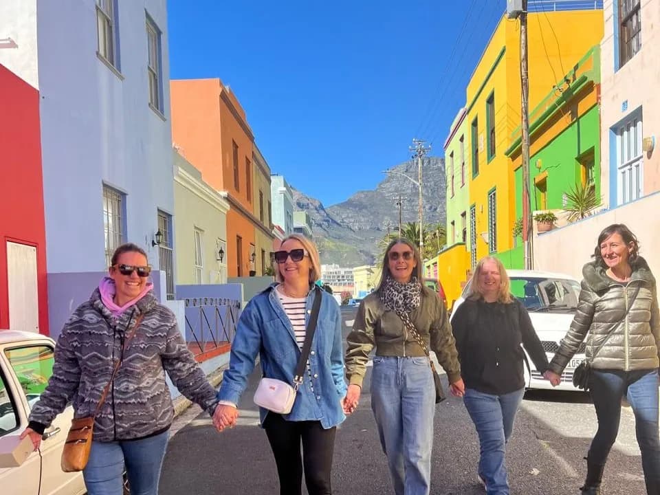 A group of travellers walking a Bo-Kaap street lined with brightly painted houses, Table Mountain rising at the end of it