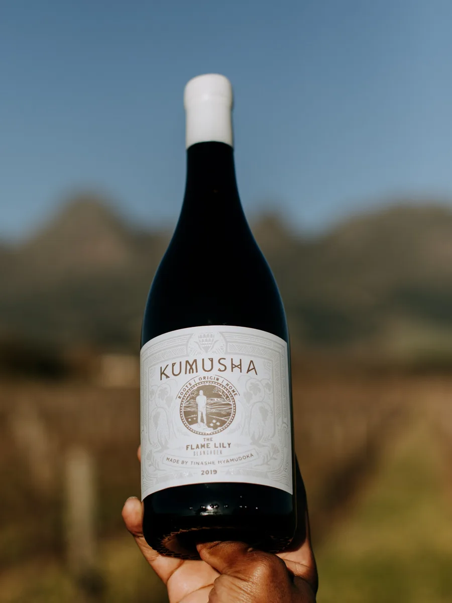 A bottle of Kumusha The Flame Lily held up against the vineyard