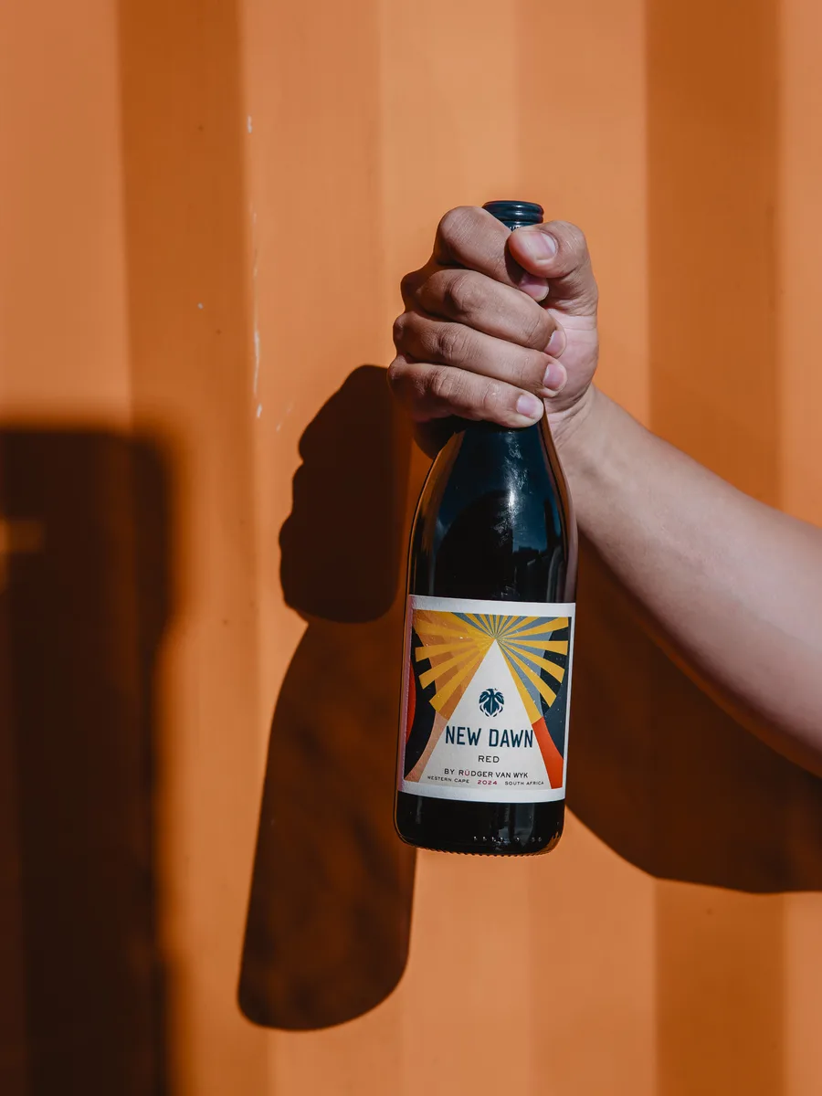 A New Dawn bottle held against a warm-toned wall